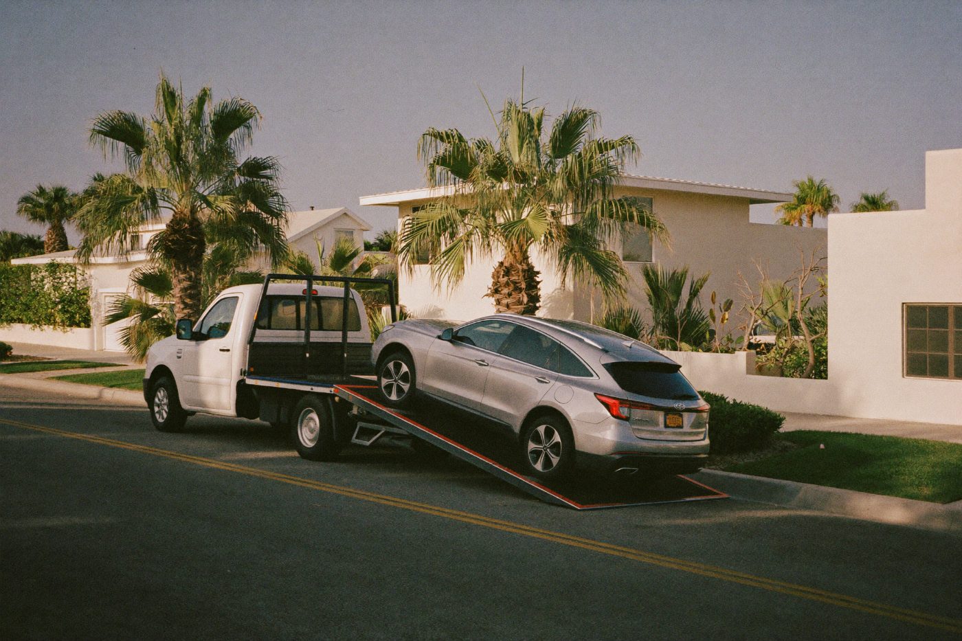 Flatbed tow truck loading a sedan on a suburban street